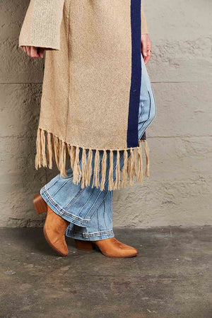 Khaki cardigan with fringe hem and navy trim, styled with flared jeans and boots.