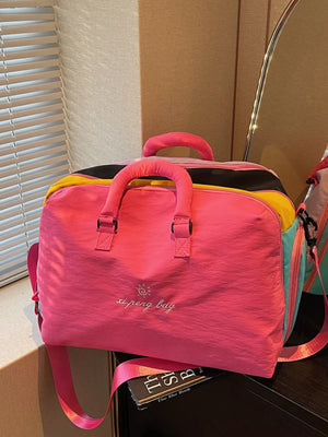 Vibrant pink duffel bag with embroidered text and multicolor accents, featuring top handles and a crossbody strap.