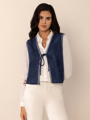 Dark blue suede-effect vest with white stitch trim and tie closure, worn over a white shirt.