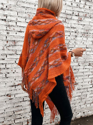 Textured knit hooded cape in terracotta with fringe and colorful stripes.