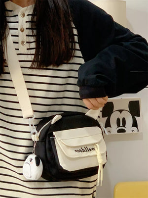 Black and white crossbody bag with cat ears and a plush charm, adjustable strap.
