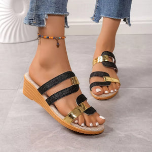 Glistening dual-strap wedge sandals in black and gold with a wooden wedge heel.