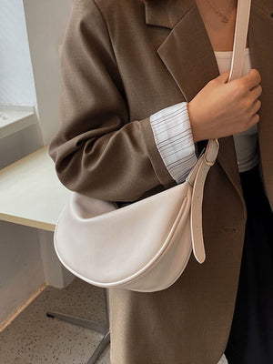 Crescent crossbody bag in beige white faux leather with adjustable strap.