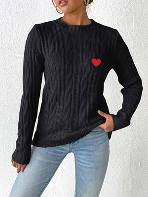 Black cable knit sweater with embroidered red heart detail.