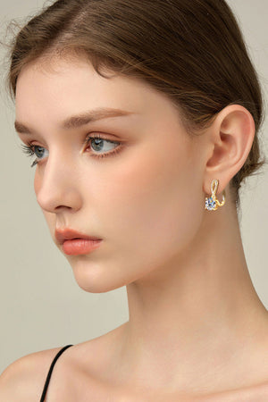 Gold crossover moissanite huggie earrings with a single round-cut stone.
