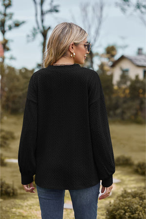 Black textured cable knit sweater with V-neck and long sleeves.