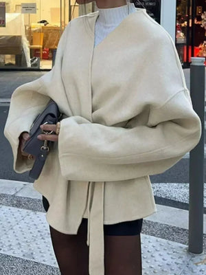 Beige belted trench coat with dropped shoulders and tie waist, styled with a clutch.