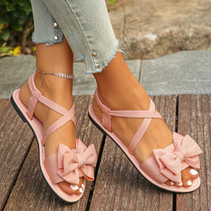 Pink crisscross bow sandals with ankle straps and a flat sole.