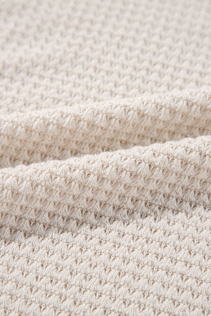Beige waffle knit V-neck top with slit hem detail.