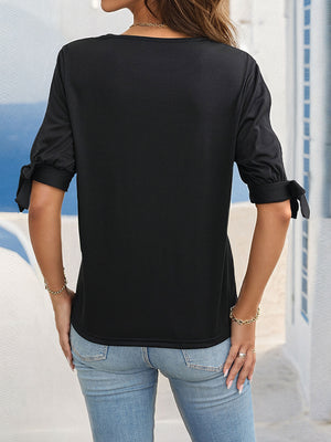 Black blouse with split sleeves featuring bow details at the cuffs.