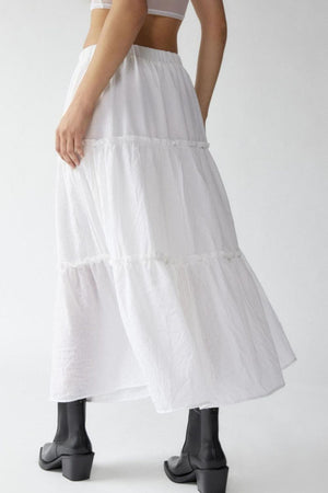 Tiered cotton maxi skirt in white with ruffled tiers, shown on a model with black boots.