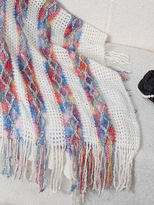 Textured knit hooded fringed cape in white with colorful diamond pattern and fringe detail.