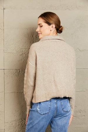 Oatmeal cable knit sweater with a zip-up collar and textured sleeves.