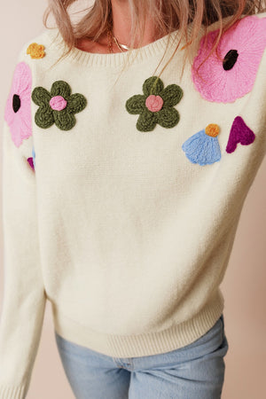 Cream knit sweater with embroidered floral appliqués and crew neck.
