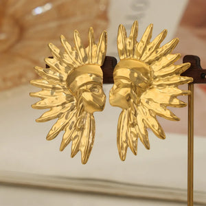 Gold sculptural statement earrings shaped like sunburst faces.