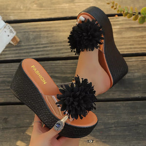 Black wedge sandals with clear straps and fluffy pom-pom detail.