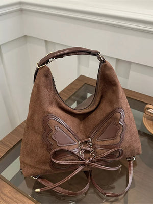 Brown suede half-moon bag with butterfly embellishment and lace-up detail.