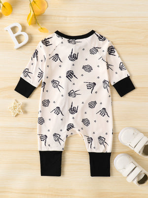 Beige baby one-piece with black skeleton hand print and stars, long sleeves, black cuffs.