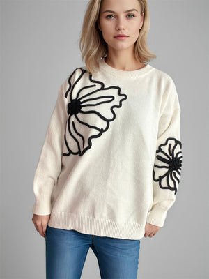 Cream knit sweater with black floral applique detail on the front and sleeve.