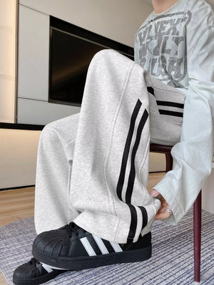 Men's light gray wide-leg sweatpants with bold black stripes down the side.