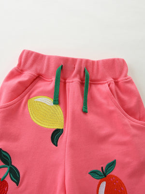 Pink cotton baby shorts with fruit embroidery and green drawstring.