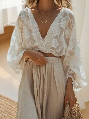 Elegant white lace crop top with deep V-neck and flowing sleeves, paired with a beige linen skirt.
