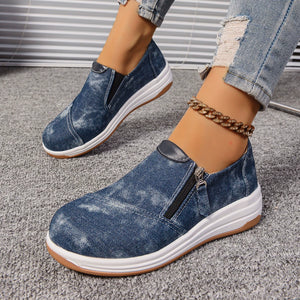 Blue denim slip-on sneakers with side zipper and chunky white sole.