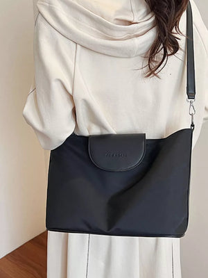 Black canvas hobo crossbody bag with a flap closure and embossed logo detail.