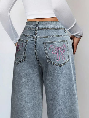Light wash denim wide-leg jeans with pink embroidered bows on back pockets.