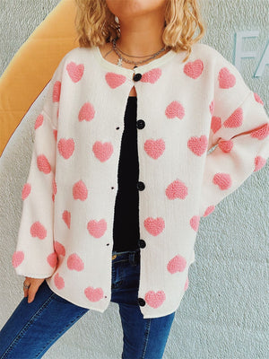 White acrylic button-down cardigan with textured pink heart motifs and black buttons.