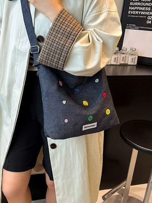 Denim crossbody bag in dark blue with colorful button embroidery and adjustable strap.