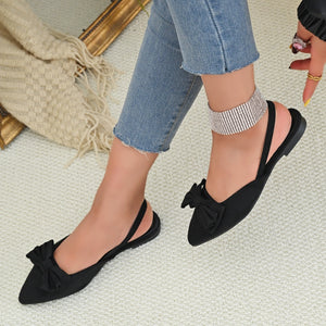 Black slingback flats with pointed toe and bow detail.