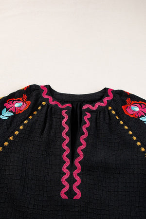 Black embroidered blouse with voluminous sleeves and pink zigzag trim.