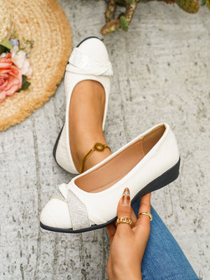 White slip-on wedge flats with rhinestone bow detail.