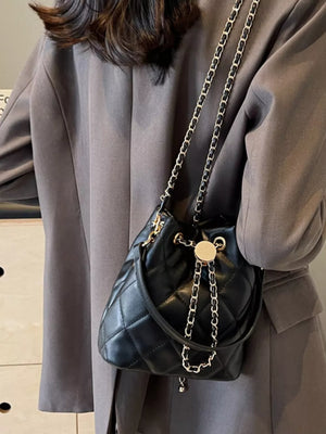 Chic quilted bucket crossbody bag in black with gold chain strap and drawstring closure.
