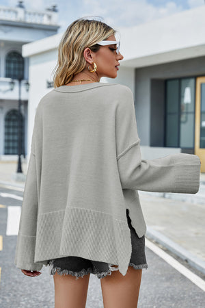 Light grey acrylic knit sweater with flared sleeves and slit hem detail.
