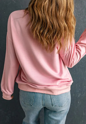 Blush pink relaxed fit sweatshirt with crewneck and long sleeves, styled with jeans.