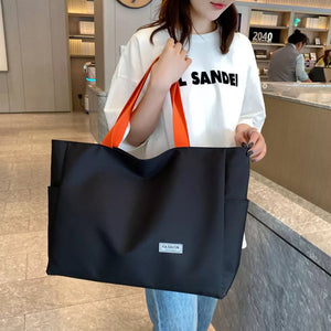 Black canvas shoulder bag with bold orange straps and side pockets.