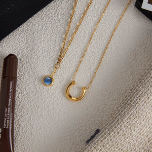Elegant gold-plated layered necklaces, one with a blue stone pendant, the other a horseshoe charm.