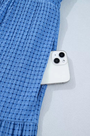 Blue tiered midi dress with a subtle checkered pattern and a phone in the pocket.