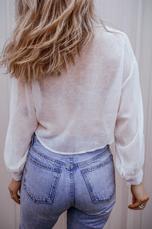 White sheer blouse with gathered sleeves and subtle textured pattern, styled with high-waisted jeans.