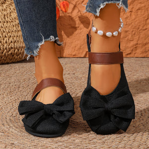 Black textured round toe flats with large bow detail and brown ankle strap.