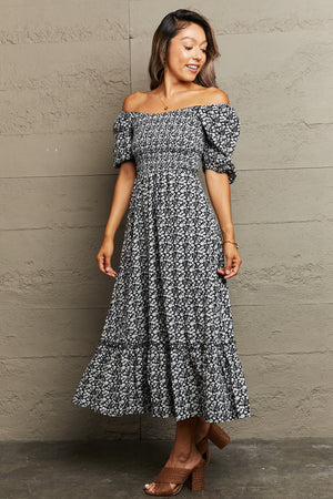 Black floral print midi dress with smocked bodice, off-the-shoulder neckline, puff sleeves, and tiered skirt.