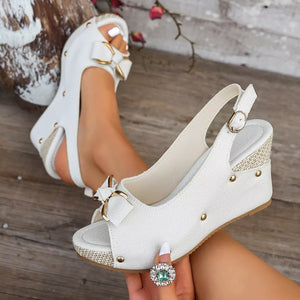 Chic white peep toe wedge sandals with decorative bow and adjustable strap.