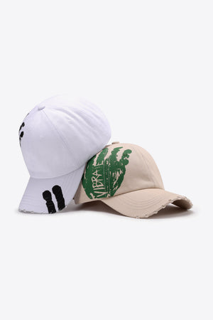 Sand baseball cap with green VIBRA graphic and distressed brim, white cap with black graphic.