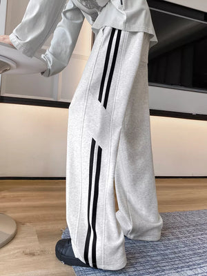 Men's light gray wide-leg sweatpants with bold black stripes down the side.