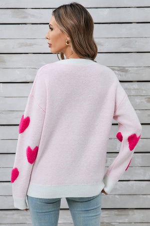 Light pink crewneck sweater with hot pink heart appliqués on sleeves.