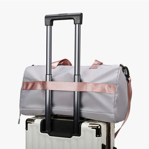 Gray duffel bag with pink strap detail and buckle, resting on a suitcase.