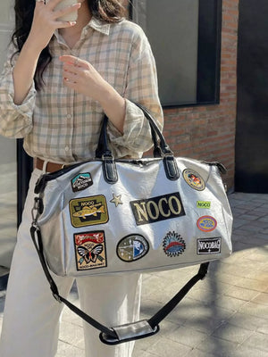 Metallic patchwork travel bag with textured finish and embroidered patches, featuring top handles and a crossbody strap.
