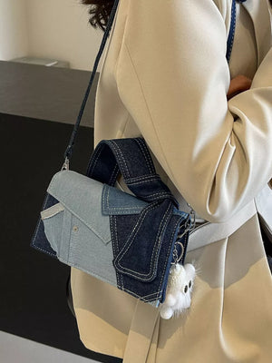Artisanal patchwork denim crossbody bag in light blue and dark blue with white stitching and a fluffy charm.